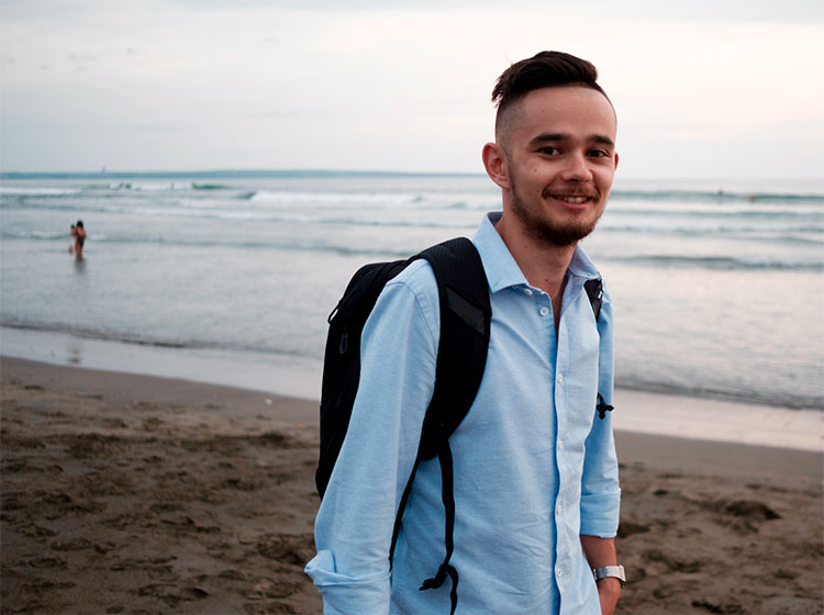 young andrey azimov with a backpack standing on a sea beach