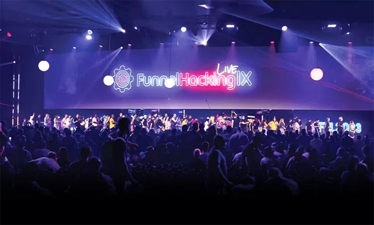 A large crowd at a conference with a stage in the background displaying "Funnel Hacking Live IX" under bright lights.