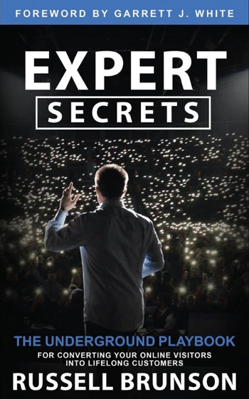 Cover of the book "Expert Secrets" by Russell Brunson, featuring a man facing an audience with illuminated devices. Foreword by Garrett J. White. Subtext reads: "The underground playbook for converting your online visitors into lifelong customers.