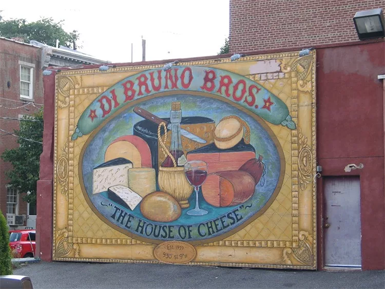 Mural of various cheeses, wine, and bread with "Di Bruno Bros. The House of Cheese" text on a brick wall.